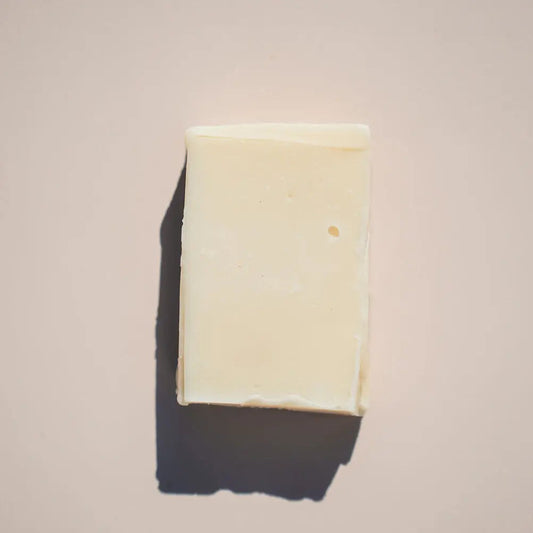 The creamy white Free Spirit Soap by Your Only Earth, exuding a subtle patchouli aroma, rests against a light beige background. It casts a soft shadow to the left, and its smooth surface with tiny imperfections enhances its natural hippie vibe.