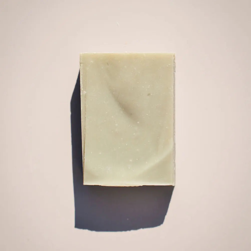 A bar of light green Lemongrass Soap by Your Only Earth rests on a plain white background, its rectangular shape and smooth texture emphasized by shadows to the left. This exfoliating bar combines fresh lemongrass aroma with gentle cleansing.