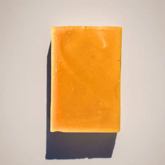 A rectangular orange Turmeric Soap bar from Your Only Earth rests on a light gray background, casting a shadow. Its anti-inflammatory properties gently care for dark spots and aging skin.