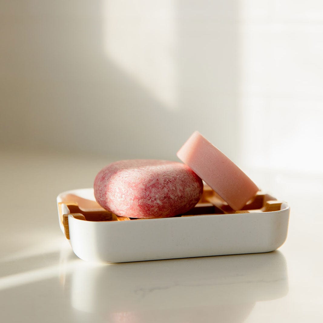 Two pink bars of soap sit on a ZeroWasteStore.com Bamboo Soap Dish with a wooden insert, displayed on a light surface in gentle natural sunlight.