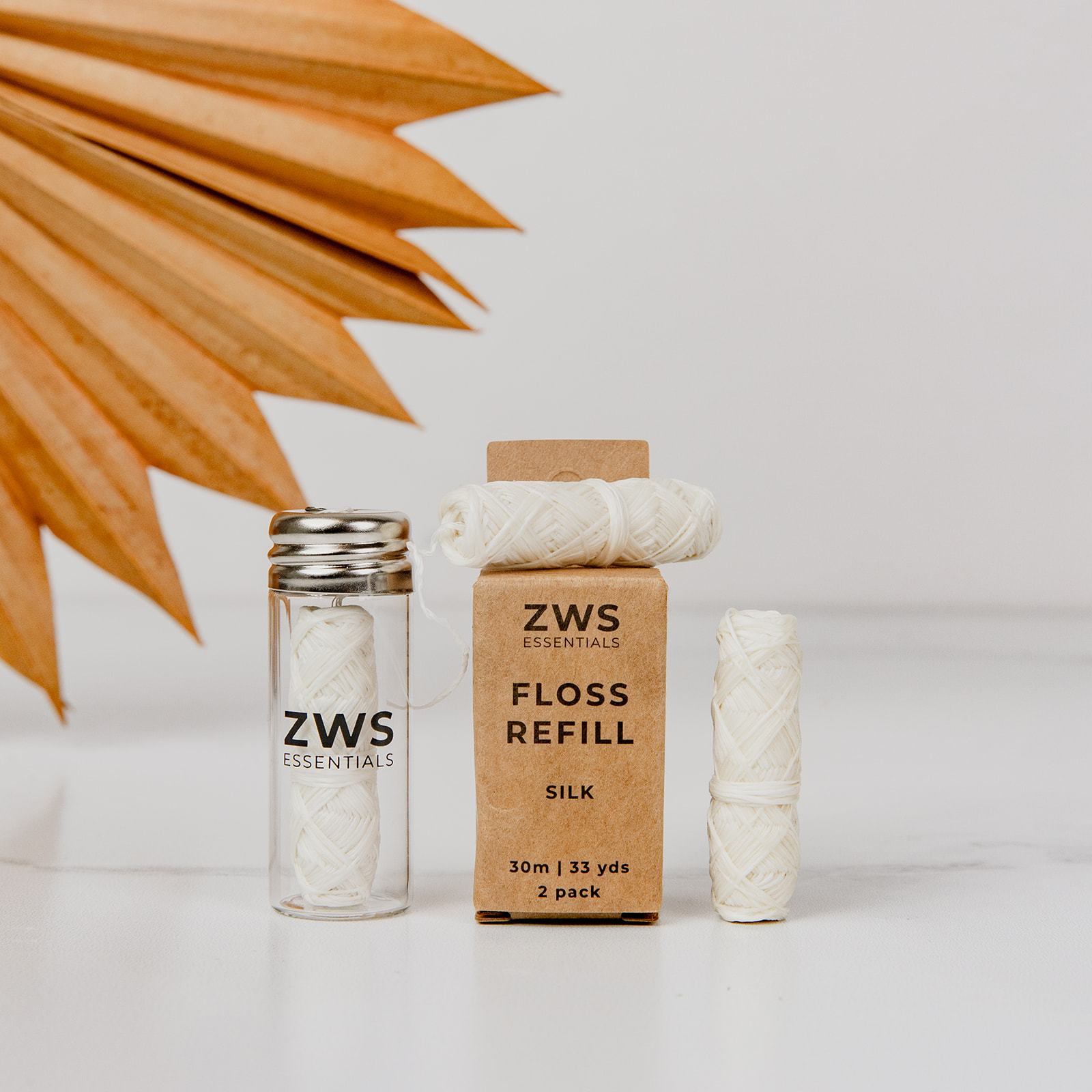 Three spools of Silk Floss - Zero Waste Dental Floss (30m, Biodegradable) from ZeroWasteStore.com are shown: one in a glass vial, one next to the refill box, and one on top. Enhanced with organic peppermint oil, they are plastic-free and eco-friendly.