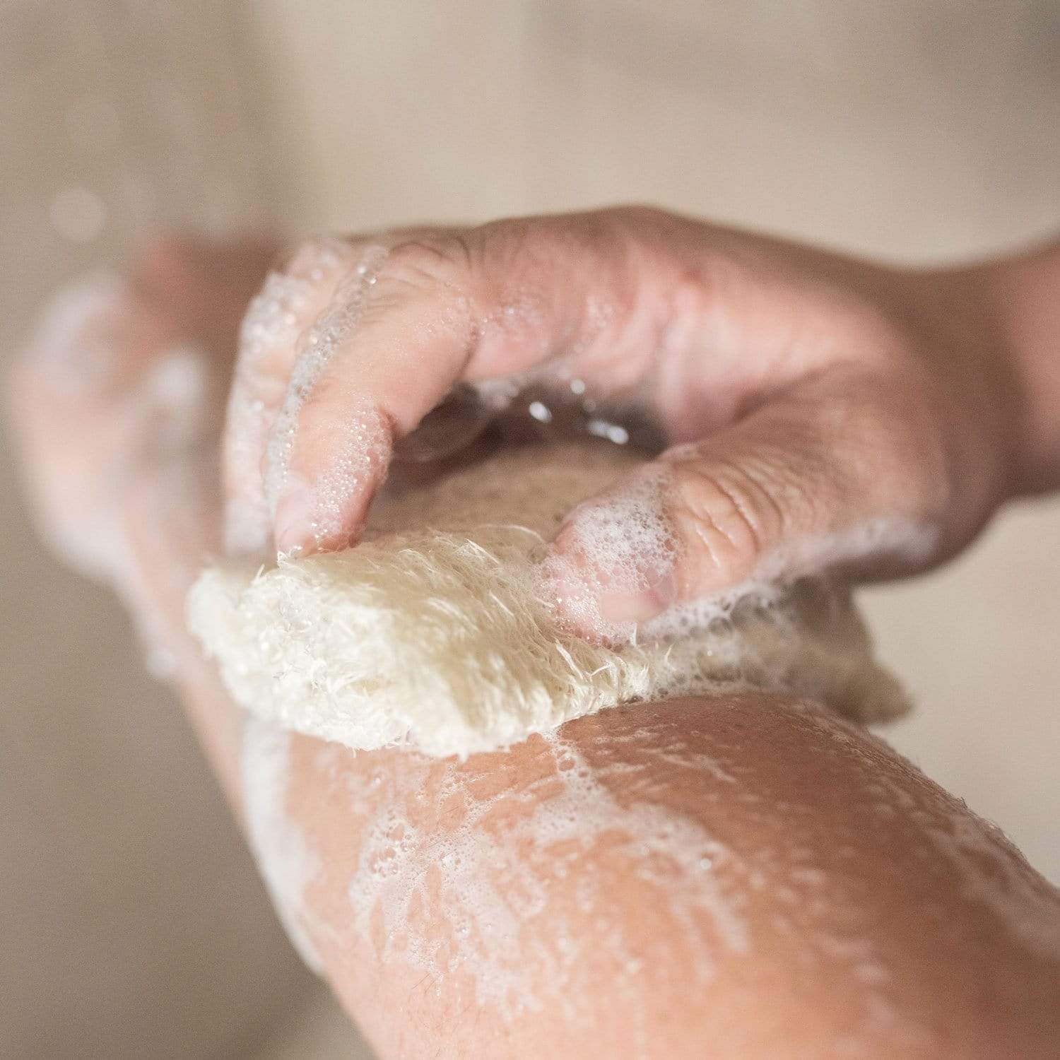 A close-up of a hand using the ZeroWasteStore.com Loofah Sponge Pack to scrub an arm, creating bubbles and foam on the skin.