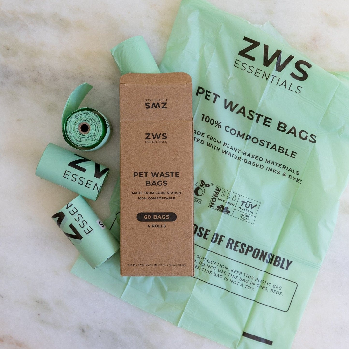 Compostable Pet Waste Bags by ZeroWasteStore.com, in rolls and a brown box labeled with the brand name, are displayed on a light marble surface.