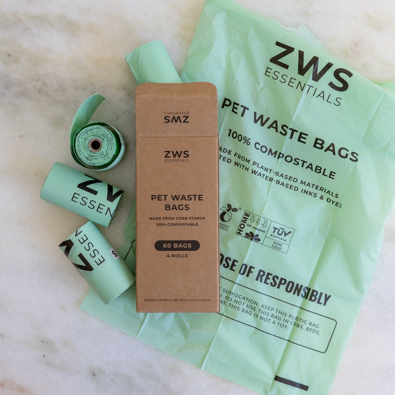 Compostable Pet Waste Bags by ZeroWasteStore.com, in rolls and a brown box labeled with the brand name, are displayed on a light marble surface.