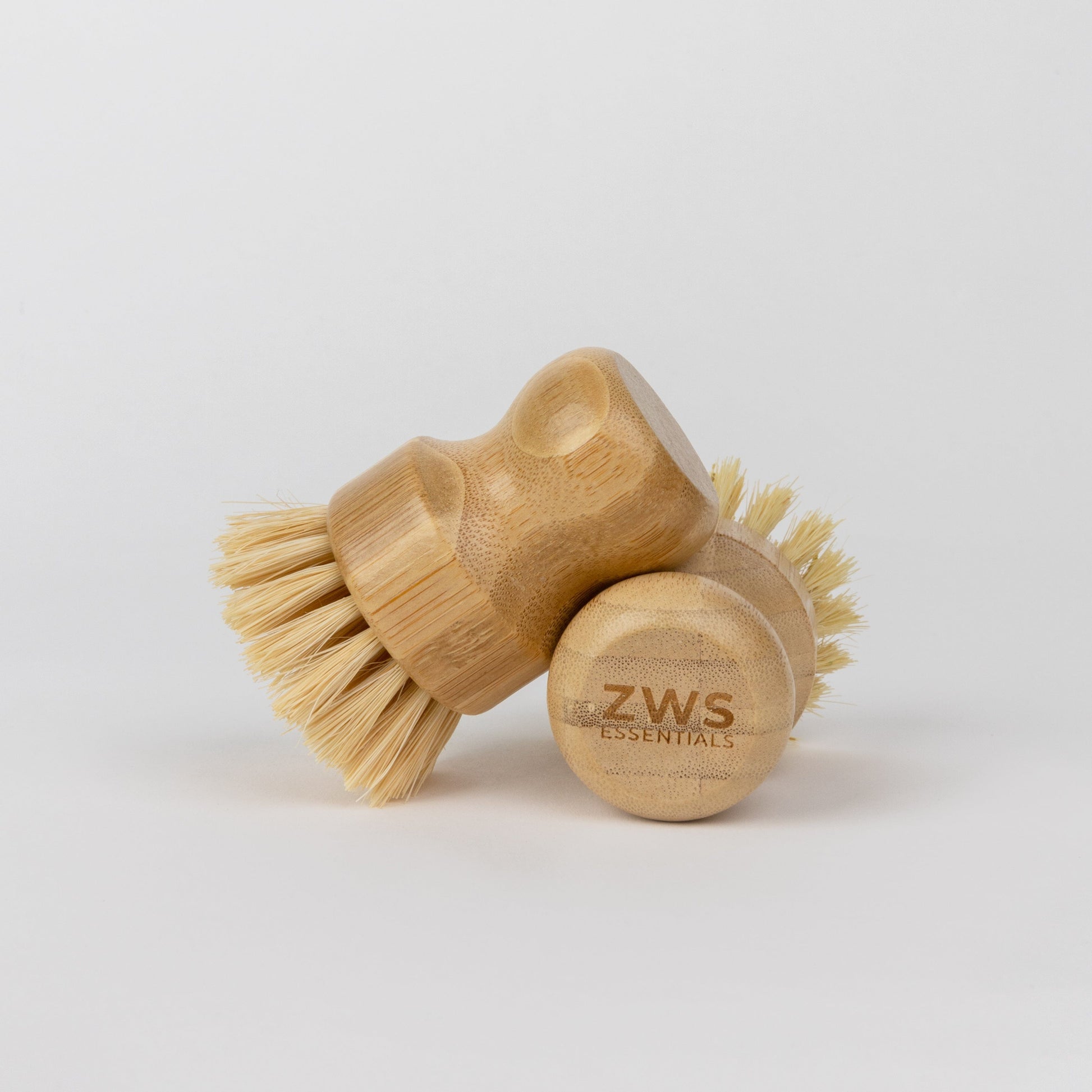 Two ZeroWasteStore.com Dish Brushes with light bristles are shown on a white background. One stands upright and the other lies on its side, revealing the logo engraved on its base—a great plastic-free dish brush option.