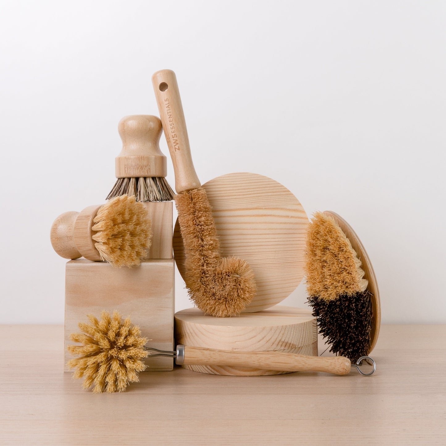The ZeroWasteStore.com Zero Waste Dish Brush Kit features natural wooden brushes with biodegradable bristles, artfully displayed on a light wooden surface against a plain white background.
