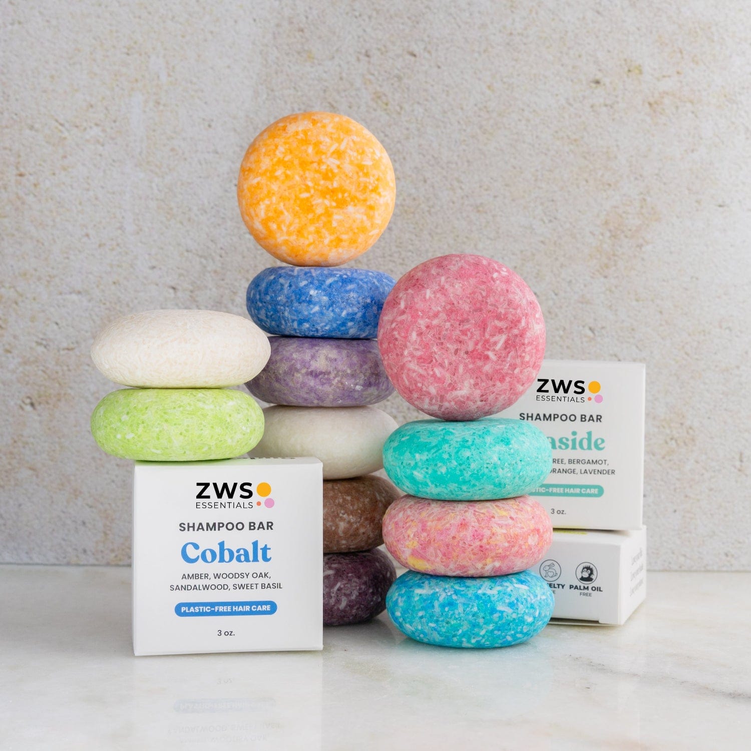 Colorful vegan Shampoo Bars by ZeroWasteStore.com are stacked in two columns beside branded boxes. These zero waste bars come in vibrant yellow, purple, green, white, pink, red, and blue.