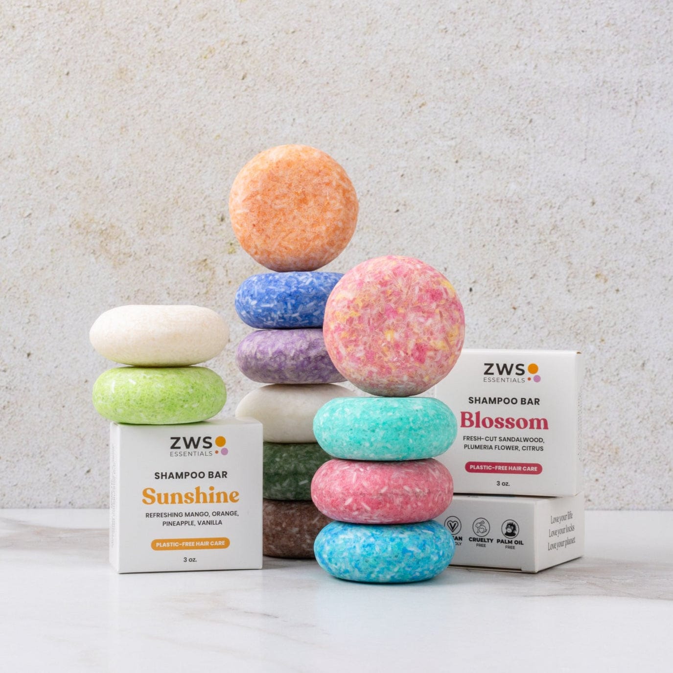 Several vibrant Shampoo Bars by ZeroWasteStore.com are stacked in towers, with two white boxes labeled Sunshine and Blossom scents, displayed against a light background.