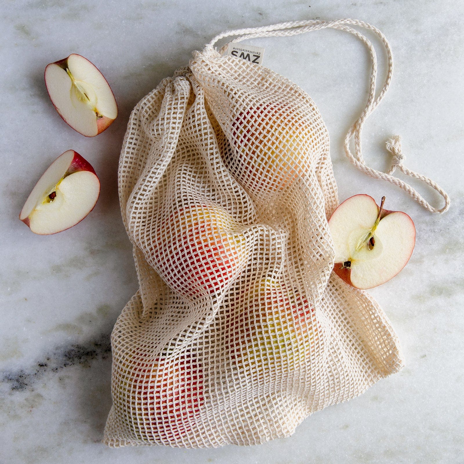The Mesh Produce Bag - Multiple Sizes - Zero Waste Net Bag by ZeroWasteStore.com, filled with apples and surrounded by apple halves on a marble surface, is ideal for a zero waste lifestyle.