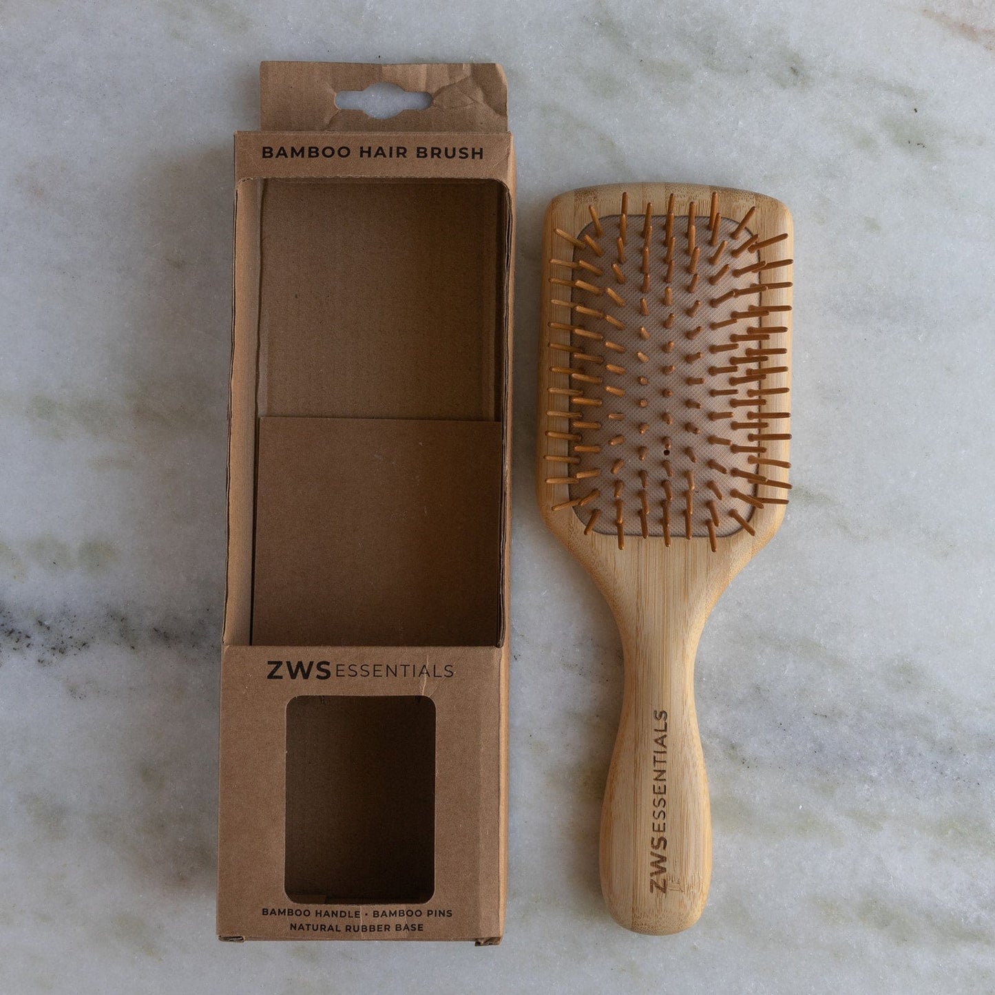 A zero waste Bamboo Hair Brush from ZeroWasteStore.com with wooden bristles sits beside its open cardboard box on a marble surface.