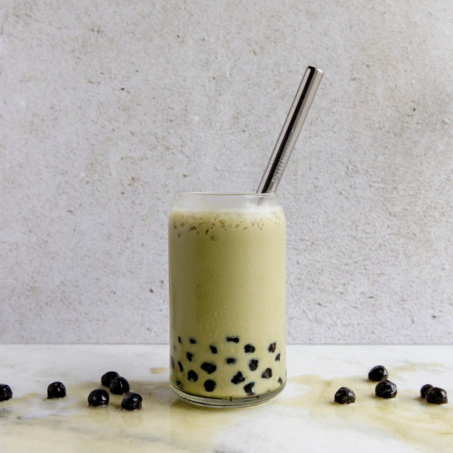Enjoy iced bubble tea with black tapioca pearls and a boba-style Stainless Steel Straw from ZeroWasteStore.com, placed on marble with loose pearls, against a light background—a plastic-free sipping experience.