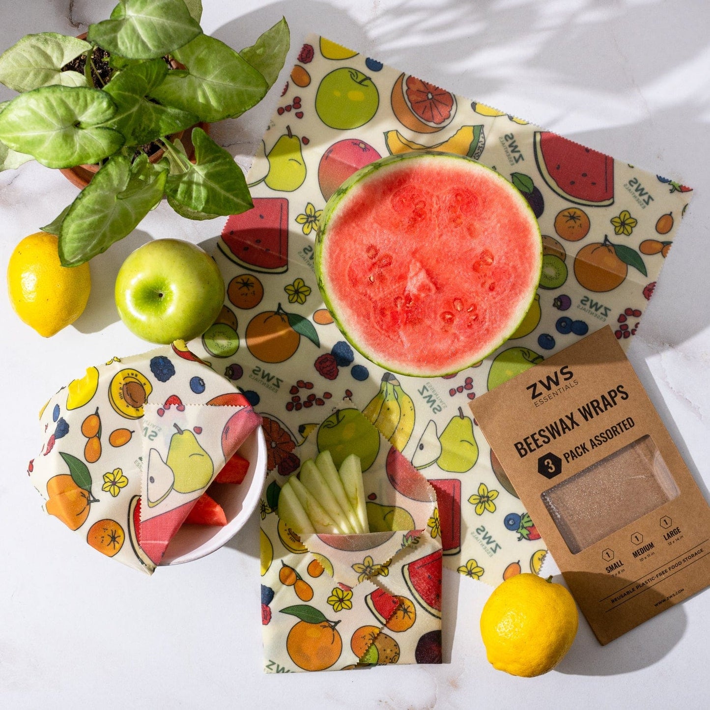 ZeroWasteStore.com's Beeswax Wraps – Plastic-Free Food Storage covers fruit bowls, watermelon, apple, lemons, and its box on a white surface—offering a bright, eco-friendly alternative to plastic wrap.