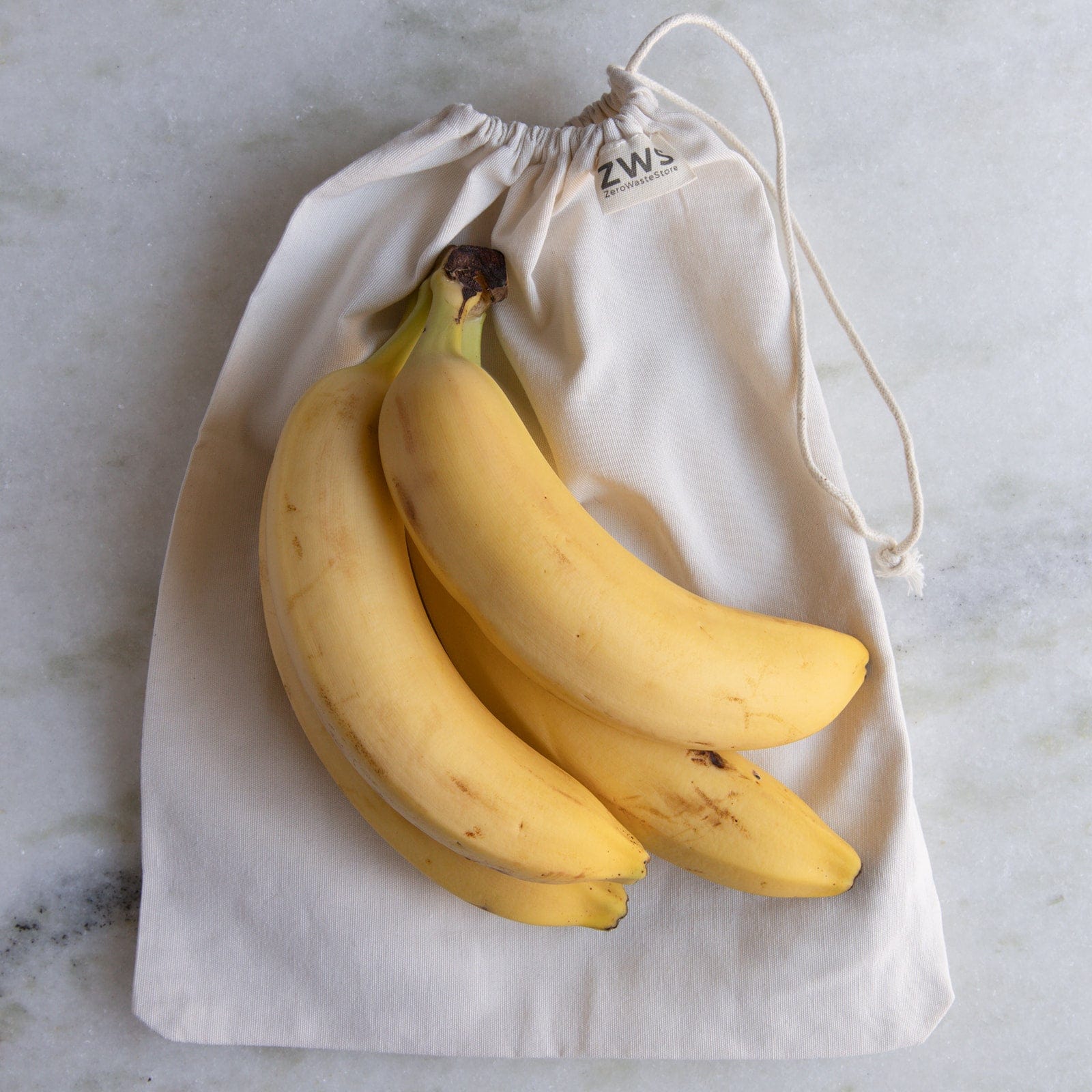 Three ripe bananas sit on a cream Muslin Produce Bag by ZeroWasteStore.com, perfect for zero waste grocery shopping. This reusable bag comes in multiple sizes for eco-friendly produce storage.