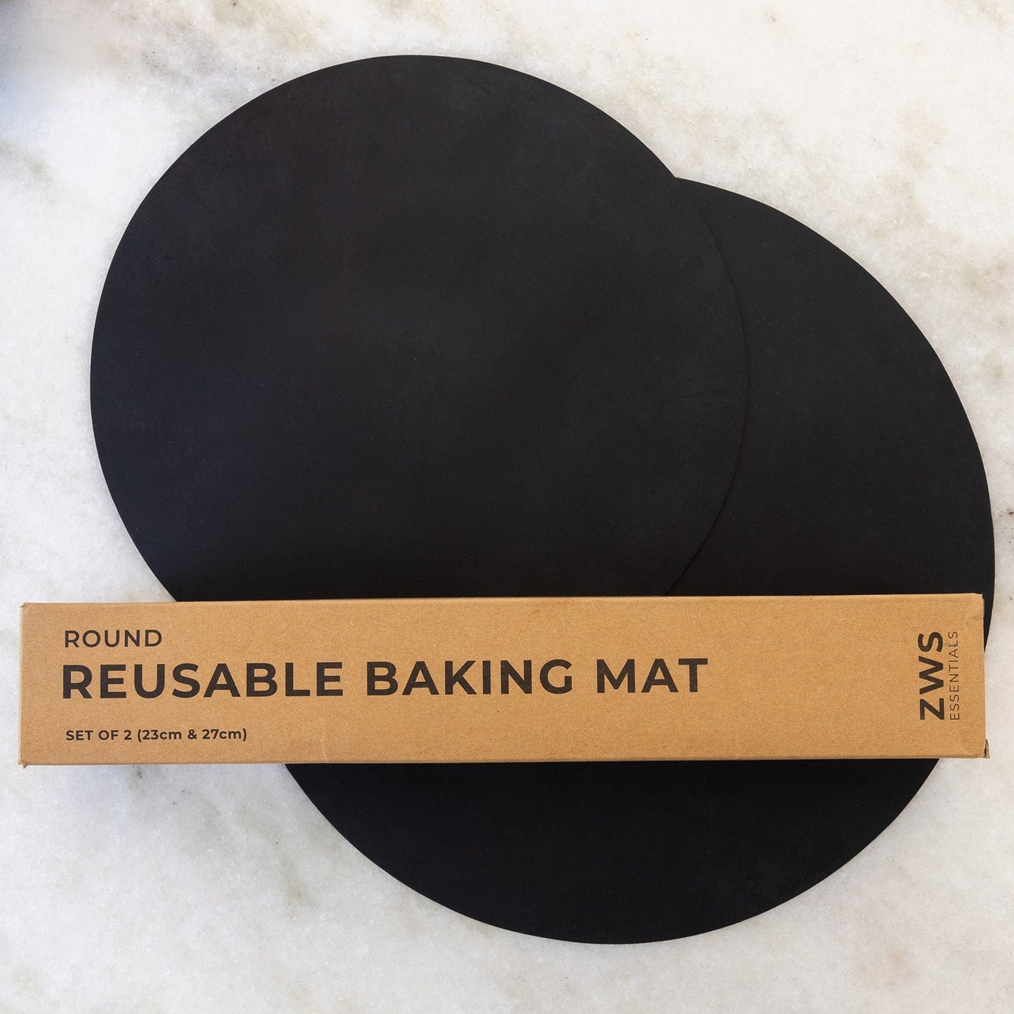 Two round black Silicone Baking Mats from ZeroWasteStore.com (23cm & 27cm) are shown on a white surface beside their brown box. These non-stick mats offer easy, mess-free baking and come as a set of 2.