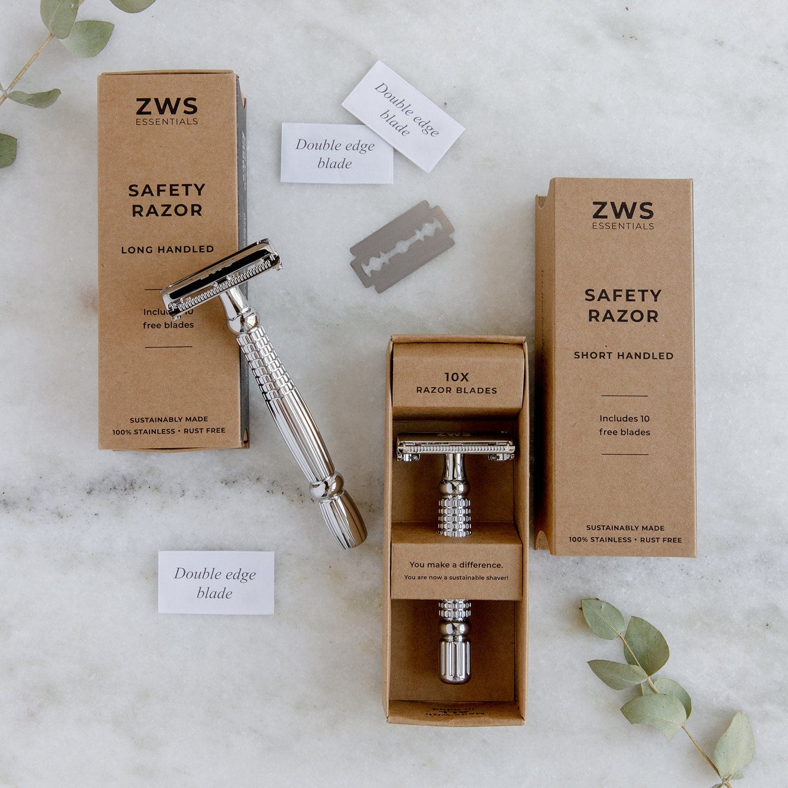 Two metal safety razors sit with ZeroWasteStore.com’s brown Zero Waste Razor Replacement Blades packaging, spare blades, and greenery on a white surface.